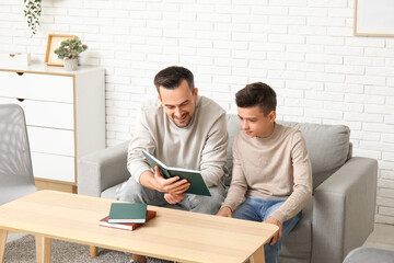 Wall Mural - Father and his little son reading books on sofa at home