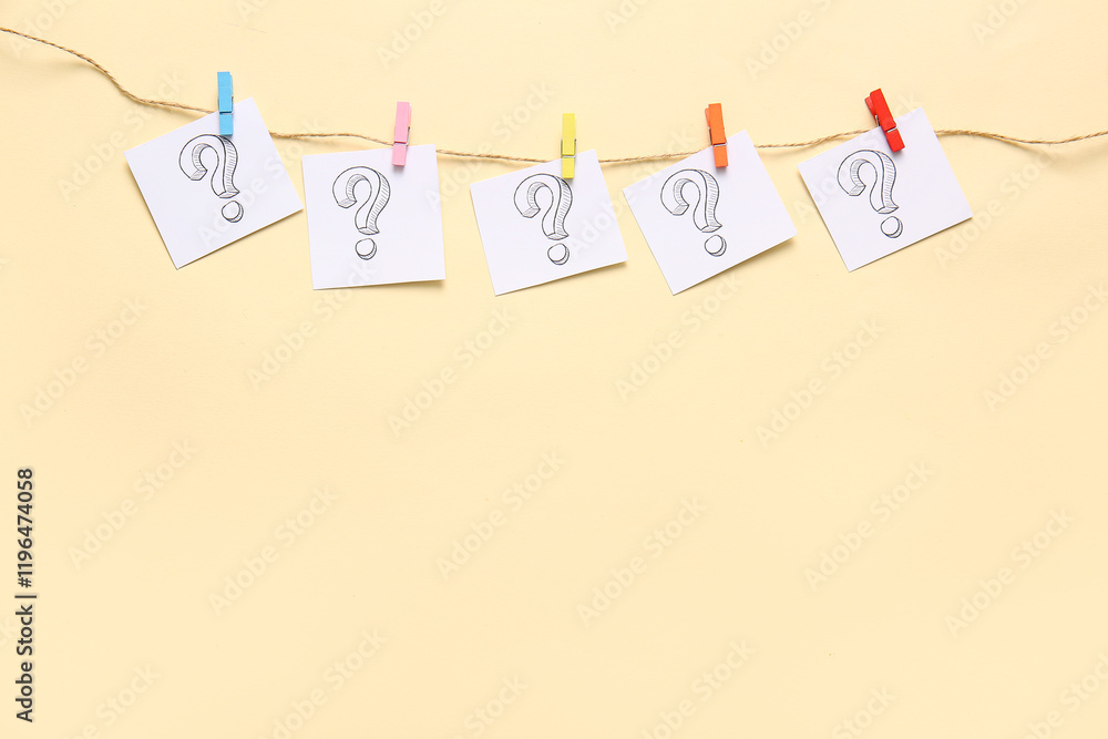 Sticky notes with question marks hanging on rope against color background
