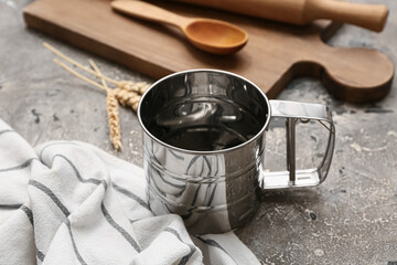 Wall Mural - Metal flour sieve mug, napkin and kitchen utensils on grunge background