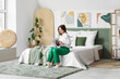 © Pixel-Shot - Young woman reading magazine near stylish paintings on light wall in bedroom