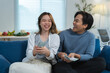 © crizzystudio - Young asian couple sitting on a blue sofa in their living room, counting dollar bills, laughing together, and celebrating their financial achievements with joy and excitement