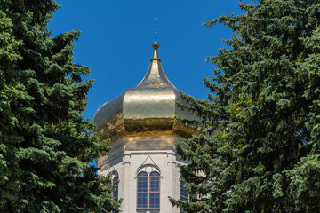 Golden Orthodox crosses on domes of Kazan Icon of Mother of God Cathedral glow in sun. Snow-white walls of cathedral with golden domes against blue May sky. Stavropol, Russia - May 23, 2024