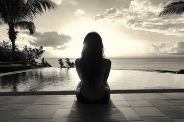 Canvas Print - Woman sits on a ledge overlooking a pool and ocean. The image has a mood of solitude and contemplation