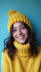 A smiling young woman with dark hair wears a vibrant yellow sweater and matching beanie, radiating warmth against a teal background. Her joyful expression and cozy attire evoke feelings of happiness