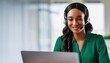 © Marko - African woman call center agent, wearing a green blouse, smiling brightly while using a headset and laptop for customer service