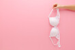 © fotoduets - Young adult woman hand holding white lace bra on light pink background. Pastel color. Female casual underwear. Closeup. Empty place for text. Front view.