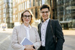 © muse studio - Young professionals with glasses stand confidently outdoors in an urban setting during daylight