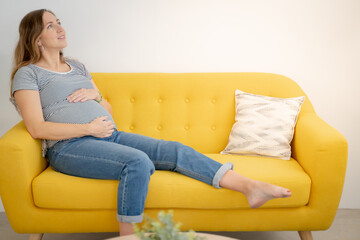 A serene and beautiful pregnant woman is enjoying a peaceful moment of relaxation on a vibrant yellow couch