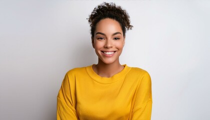 A cheerful young woman with curly hair, wearing a bright yellow sweater, smiling warmly at the camera. Simple, natural portrait on a light background, perfect for lifestyle or positive-themed designs.