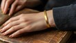 © Nuttaya Nampai - Elegant gold bracelet showcased on a woman's wrist, her hand gently resting on a book with warm light creating a cozy, luxurious vibe.
