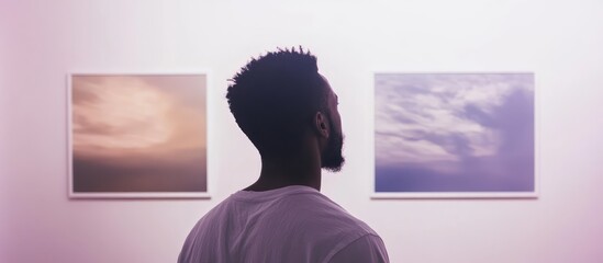 Black man observing digital art in a gallery, two framed images on wall