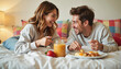 © Elenba - Playful couple laughing while enjoying breakfast in bed, cozy atmosphere