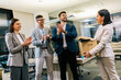 © Mediteraneo - Happy business woman approaching her table at the new job that she got hired. She has a box with personal stuff. Her colleagues applause and congrats her.