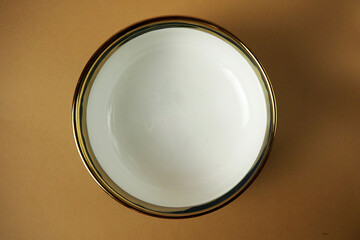 top view of white inside soup or dessert plate bowl with gold coating on top on brown background . empty tableware