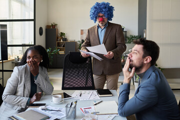 Poster - Young intercultural white collar workers laughing at mature boss wearing blue clown wig, red nose and formalwear