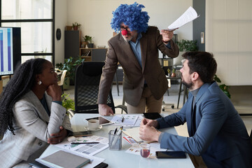 Poster - Mature confident director of business company in clown wig looking at young female subordinate during discussion