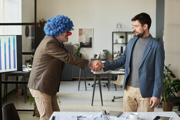 Poster - Side view of mature clown director of business company shaking hand of young male employee after signing agreement