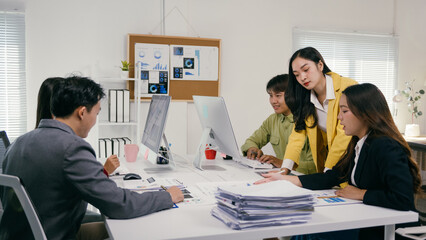 Fototapete - Group of young asian businesspeople working together, analyzing financial data on computer and documents, collaborating and discussing strategies during a productive office meeting