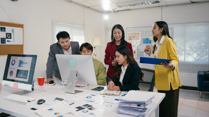 Wall Mural - Five asian businesspeople working together in modern office, analyzing charts and graphs on computer screen during collaborative team meeting