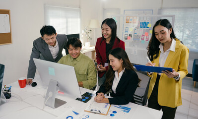 Wall Mural - Five asian businesspeople are working together on a project, using a desktop computer and analyzing charts and reports in a modern office environment