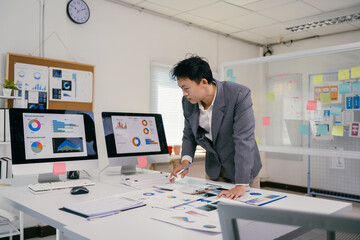 Wall Mural - Businessman analyzing financial charts and reports on desk in office meeting room, using computer and documents to study company performance and plan business strategy