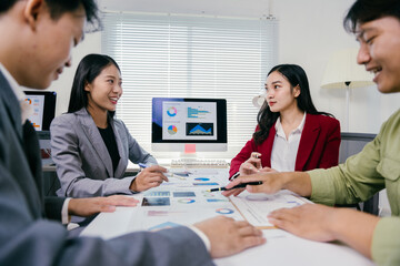 Wall Mural - Asian businesspeople discussing and analyzing charts and statistics displayed on a computer screen and printed documents, working together in the office for a successful business strategy