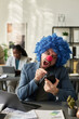© pressmaster - Young male clown manager screaming to person on smartphone screen while communicating in video chat by workplace