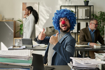 Poster - Young successful office worker in clown wig and nose looking at camera and showing thumbs up while sitting by workplace