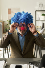 Poster - Mature surprised clown boss in eyeglasses sitting by workplace in office and working with financial documents or data