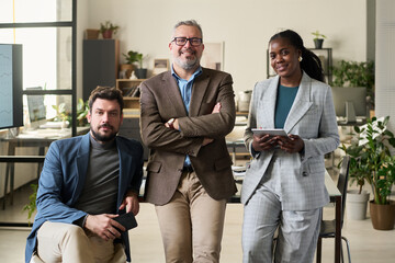 Poster - Group of successful intercultural subordinates and their boss in formalwear looking at camera while standing in coworking space