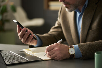 Poster - Hands of mature male boss in formalwear sitting by workplace, texting in mobile phone and making notes in notebook