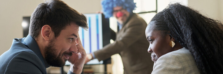 Poster - Header of young smiling subordinates looking at one another while making fun of their boss wearing clown wig during presentation