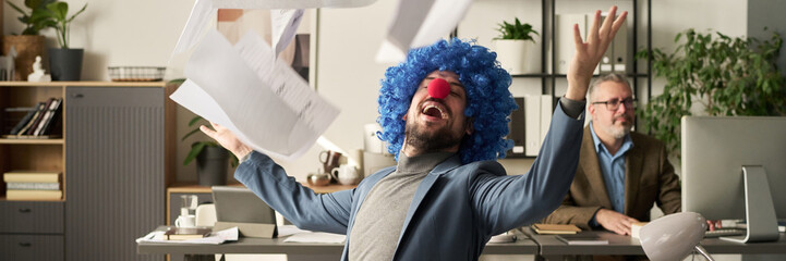 Poster - Header of young ecstatic clown male economist throwing financial paper documents over himself while sitting by workplace with laptop