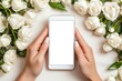 © Tondone - A serene moment featuring hands holding a smartphone surrounded by beautiful white roses. The device has a blank screen, ideal for showcasing apps or personal content.