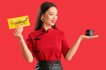 Canvas Print - Young Asian woman with greeting card for Chinese New Year and teapot on red background