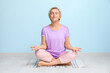 © Pixel-Shot - Portrait of meditating mature woman sitting on floor against blue wall