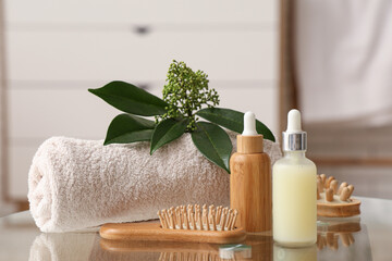 Bottles of cosmetic oil, bath supplies and green leaves on table in bathroom, closeup