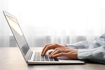 Woman working with modern laptop at wooden table, closeup