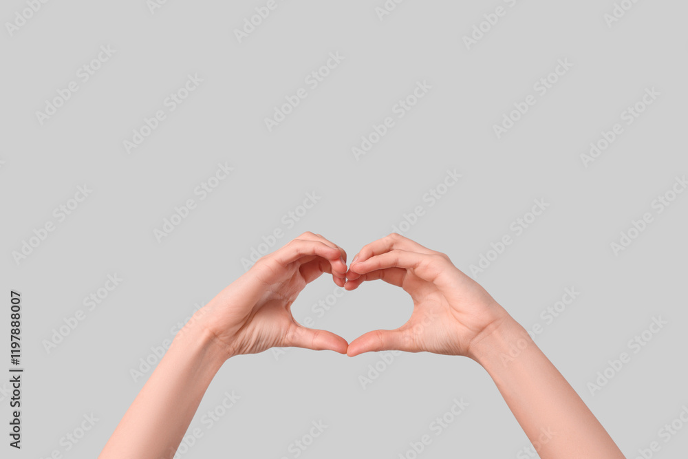 Young woman making heart with her hands on grey background, closeup