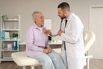 Poster - Male doctor with stethoscope listening to mature woman in clinic