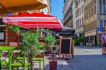 Wall Mural - Street restaurant with tables and chairs on narrow street, road with paving stone, old buildings in Antwerp historical city center, street cafe in old town Antwerpen, Belgium