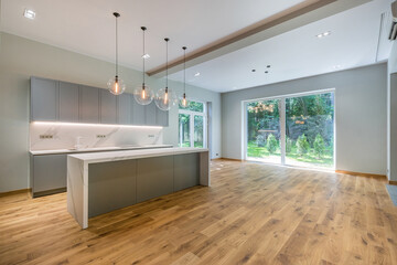 The interior of a modern private house with panoramic windows. Brown laminate floor. .Kitchen set and round ceiling lights above the table.