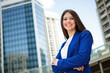© Minerva Studio - Businesswoman smiling with folded arms in front of office buildings