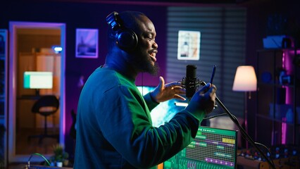 Fototapete - Young artist singing his new song creation on microphone gear, editing his recordings to adjust volume levels with mix and master techniques. Singer composing a melody, stereo tools. Camera B.