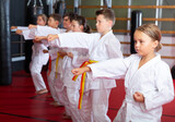 Group of young girls and boys in kimono doing kata in gym.