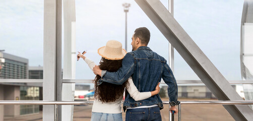 Wall Mural - Couple With Suitcases Looking Out Of Window At Airport While Waiting For Flight, Rear View Shot Of Young Arab Spouses Travelling Together, Standing With Luggage At Terminal And Pointing Away