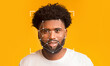 © Prostock-studio - A young man with curly hair smiles while facial recognition technology analyzes his features against a bright yellow background. The digital overlay showcases points of identification.