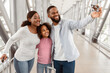 © Prostock-studio - Waiting For Flight. Portrait Of Cheerful Young Black Family Taking Selfie With Smartphone In Airport Terminal, Father Holding Cellphone. Tourists Posing For Photo Together, Blurred Background