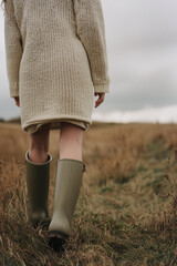 Wall Mural - woman wearing rubber boots, walking outdoors, cloudy sky on background