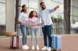 © Prostock-studio - Travelling Together. Happy Young Black Family Standing Near Airport Building Holding City Map After Arrival To New Country, Cheerful People Planning Travel Route, Man Pointing Aside, Showing Way